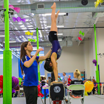 Maximum Coach assists an athlete on the balance beam at a competition.